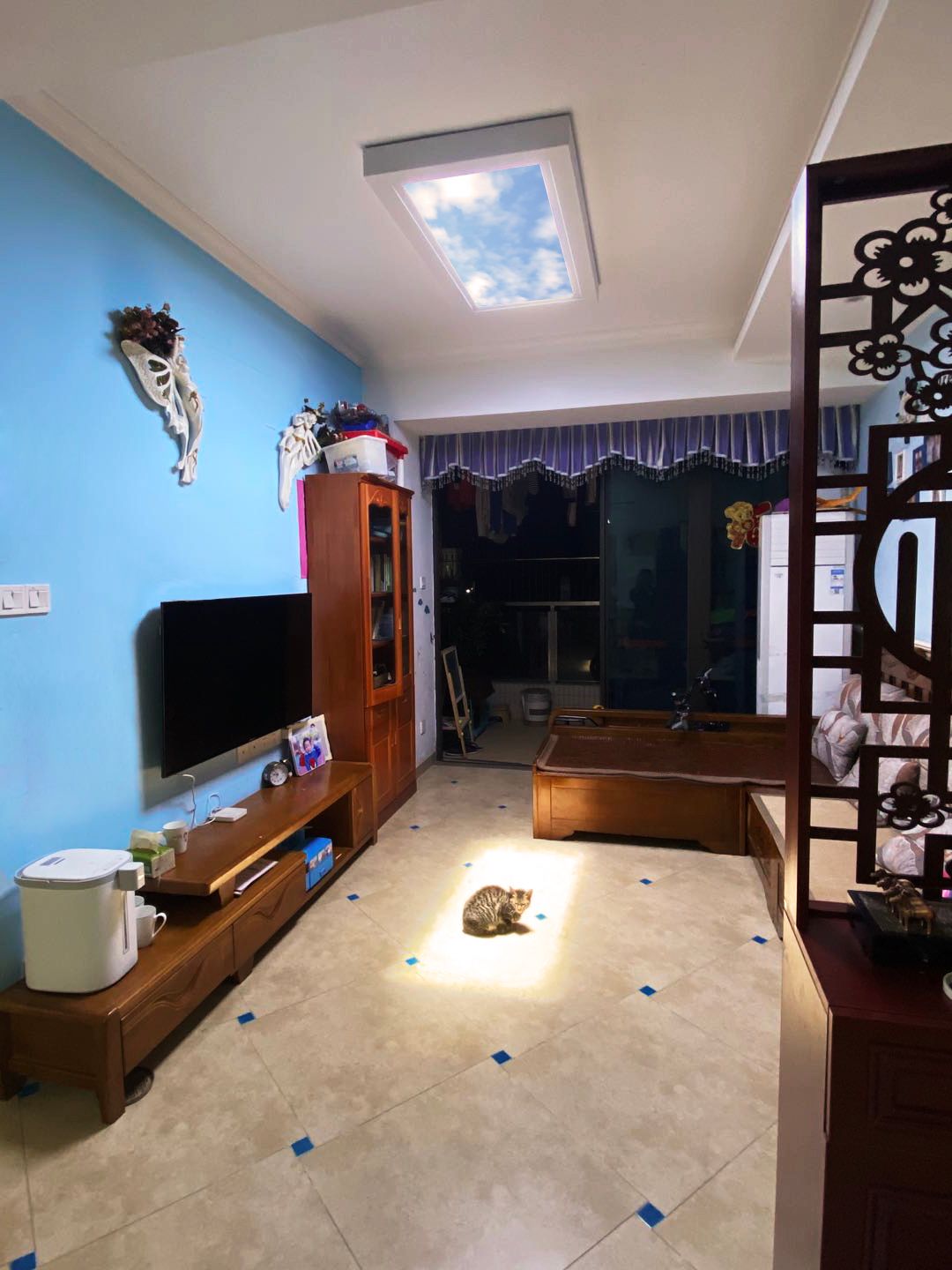 Surface-mounted blue sky skylight above a log cabin-style living room, adding natural light beside the fireplace and TV.