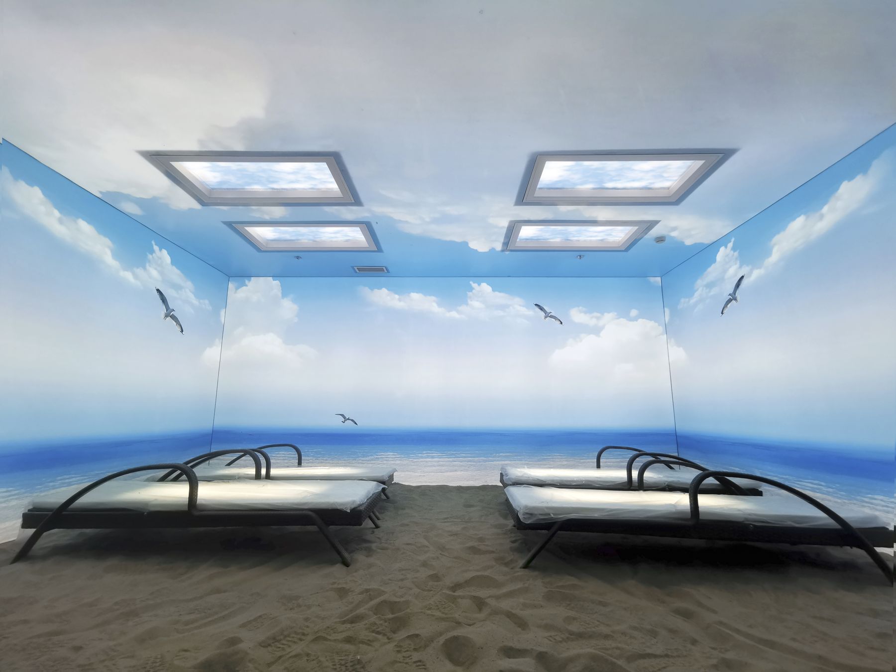 Second angle of the beach-themed light-therapy room, showing four skylights above the lounger beds.