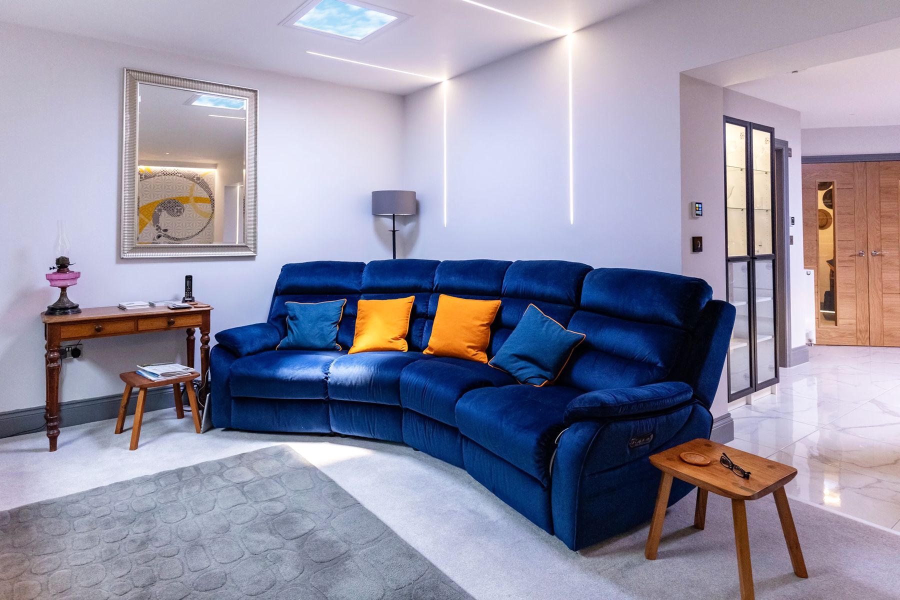 Static cloud skylight above a modern living room, paired with cove lighting to give a compact seating area a bright, natural daytime feel.