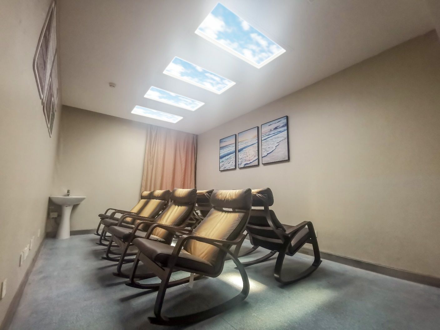 A second hospital light-therapy recliner room, with four skylights and framed beach photography reinforcing the calming, restorative feel of the space.
