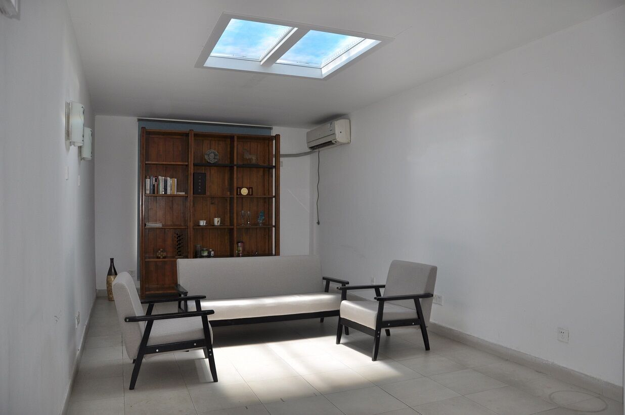 Two static cloud skylights above a living room furnished with a display cabinet and armchairs, adding daylight to the space.