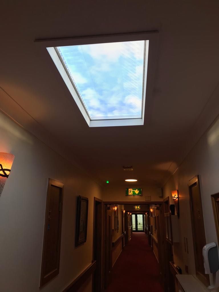 1200x600mm static cloud artificial skylight in a retirement village corridor, brightening a windowless hallway and giving residents a natural day/night cue as they move through the building.