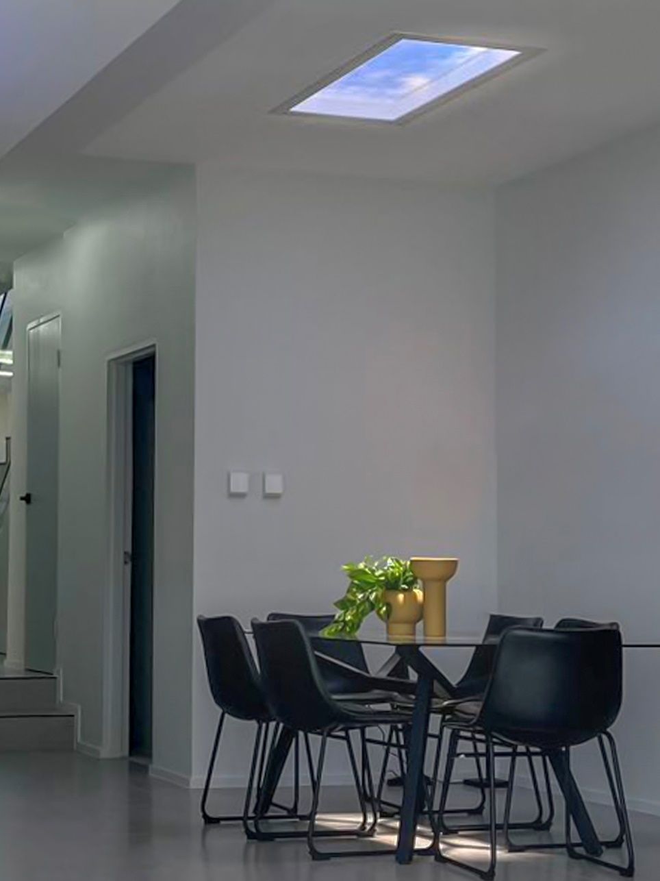 Static cloud skylight above a minimalist dining table, giving the space natural-feeling light without a nearby window.
