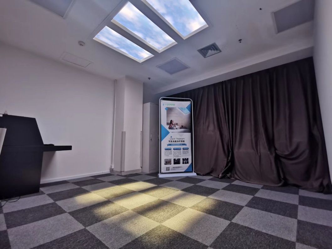 Three static cloud skylights above a hospital light-therapy room fitted with recliner chairs, delivering the kind of daily light dose used to help treat Seasonal Affective Disorder and related low-mood conditions. Static cloud was chosen over a dynamic sky here because light therapy relies on a steady, even light level for a set session length - a fixed cloud image gives consistent brightness across the room, where a moving or dimming dynamic display could interrupt the measured light dose the therapy depends on.