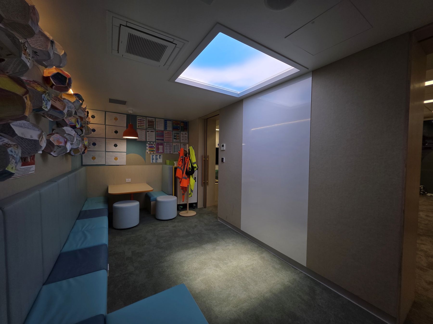 Second angle of the same primary school breakout area, showing the 1200x1200mm dynamic sky skylight above a colourful lounge, storage and quiet-play zone used by students between classes. As a dynamic sky panel, it also offers slow-moving clouds, an optional starry night mode after dark, and an adjustable colour temperature from crisp all-white daylight through to a warmer all-warm tone, letting the space be tuned through the day and evening rather than staying fixed like a static image.